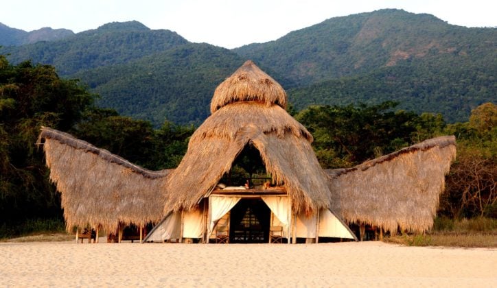 Exterior of Greystoke Mahale constructed of recycled dhows and thatched palm leaf roof set in front of the Mahale Mountains, Tanzania