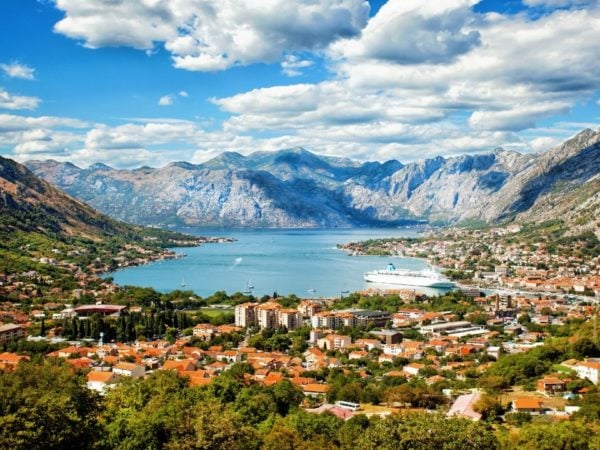 View of a bay in Montenegro - blue water surrounded by mountains, with a cruise ship docked by a small town