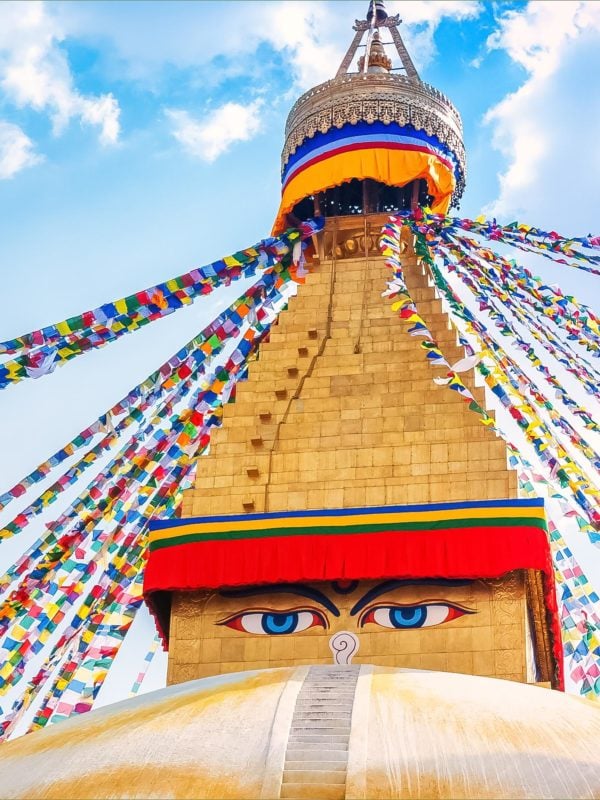 Boudhanath Stupa , a colourful temple with golden accents, two blue eyes painted on the front and hundreds of small colourful flags cascading down the side in Kathmandu valley, Nepal