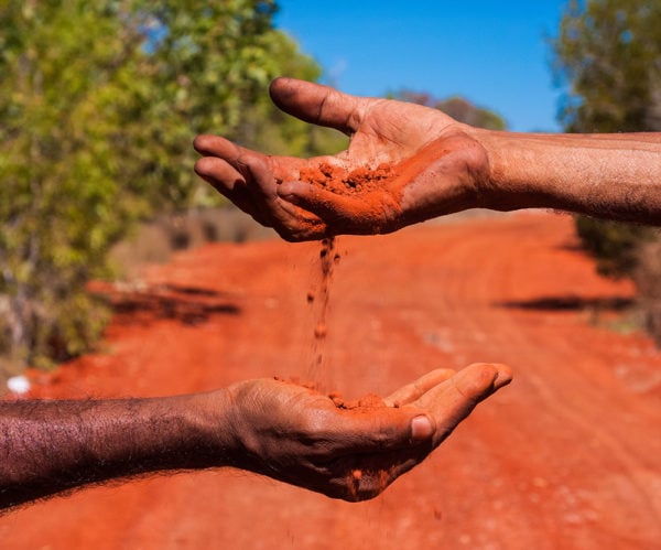 Two hands passing red dirt between them