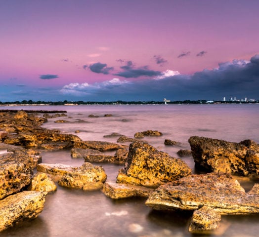 Sunset over a rocky coastline with the city of Darwin in the distance