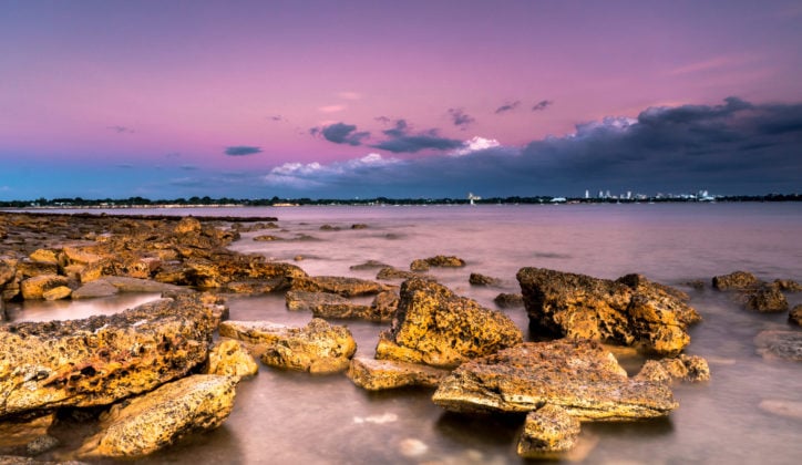 Sunset over a rocky coastline with the city of Darwin in the distance