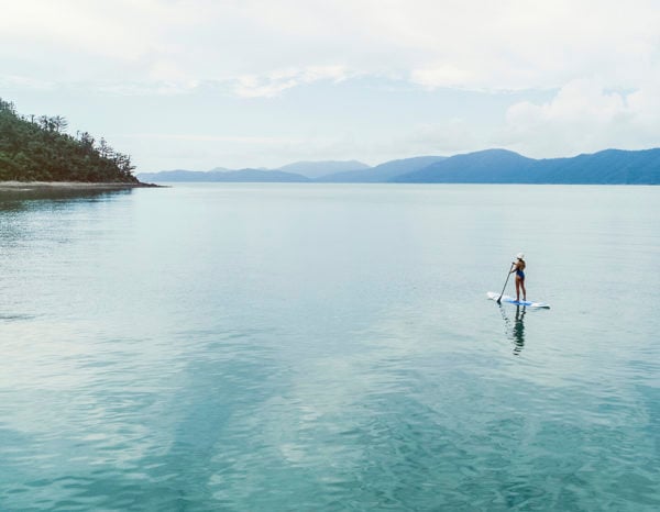 A woman standing on a paddle board paddling through still water