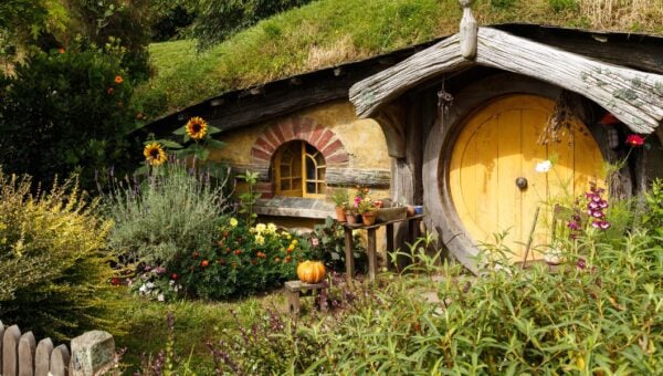 A round yellow door on a wooden Hobbit hole with blooming spring front garden in Hobbiton Movie Set, New Zealand