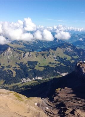 Aerial view of small grass-covered mountains and valleys in Switzerland with alpine lakes, and white fluffy clouds