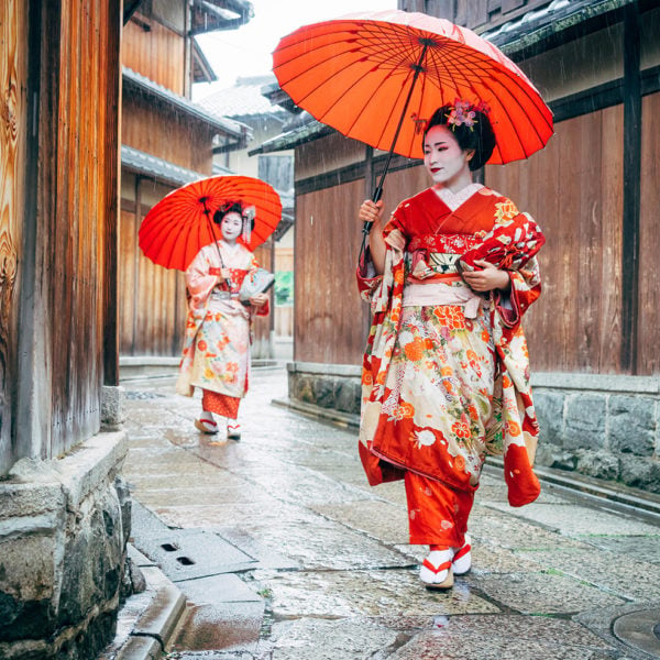 Maiko Women in traditional kimono clothing holding red parasols Walking in a rainy Kyoto