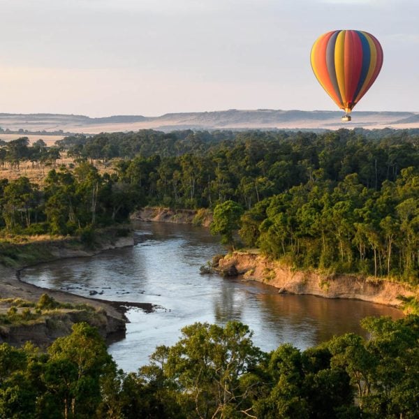 A rainbow striped hot a air balloon drifting over a river and forest