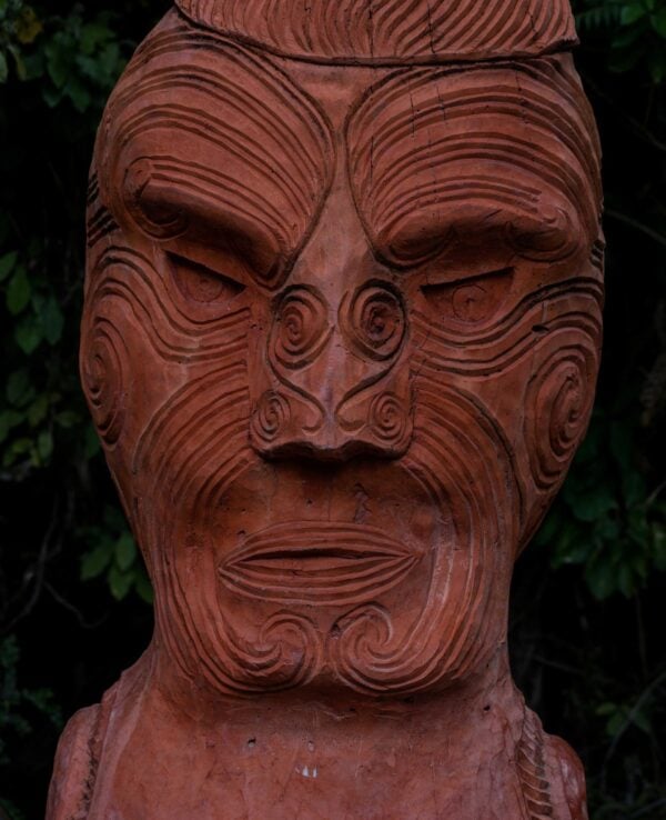 Close up portrait of traditional ancient red wooden Maori sculpture figure in Abel Tasman National Park Nelson Tasman South Island of New Zealand