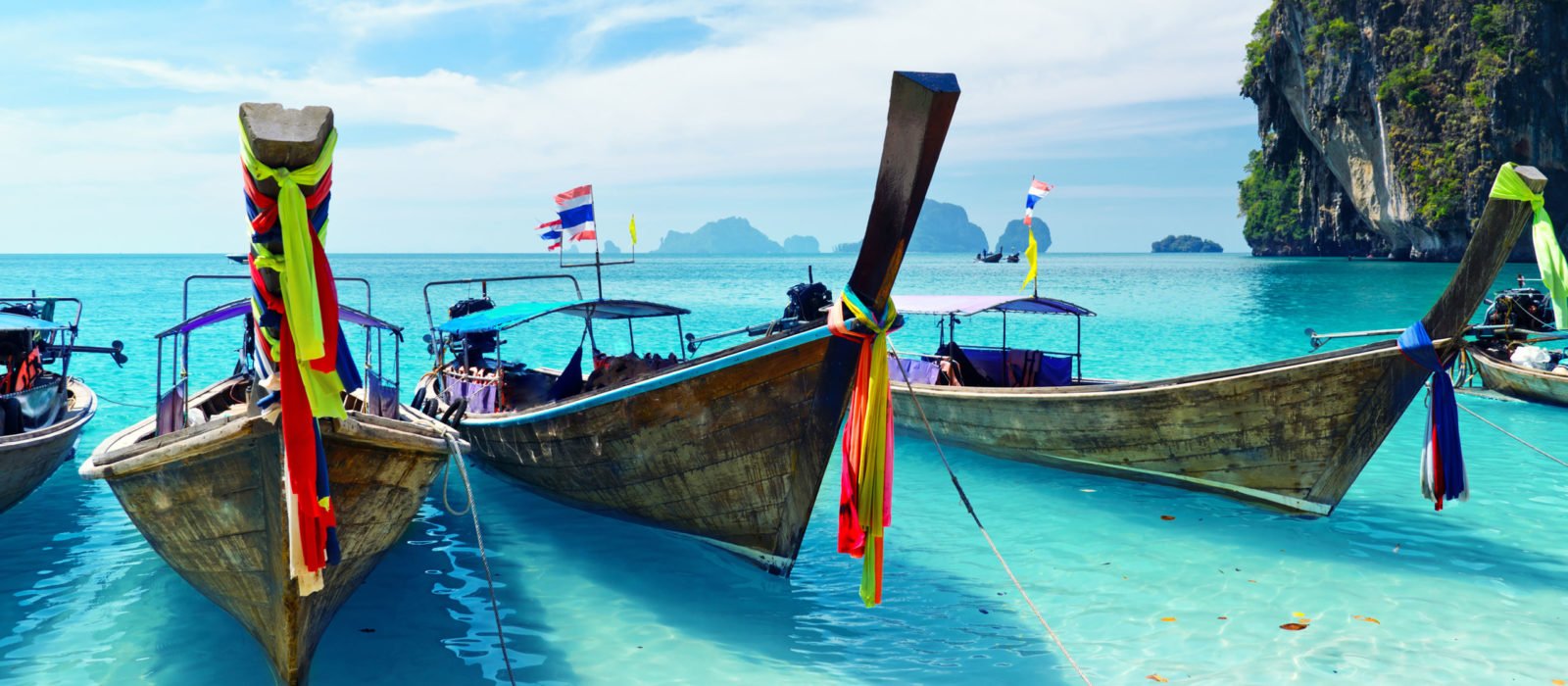 Long tail boats lined up along in shallow water in a bay in Thailand