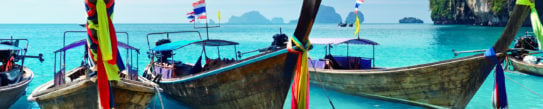 Long tail boats lined up along in shallow water in a bay in Thailand