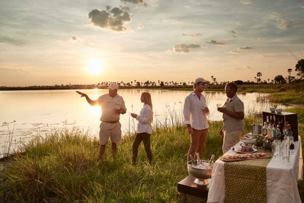 People standing by a watering hole enjoying a drink and picnic at sunset